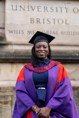 Female student in graduation gown outside an old stone building